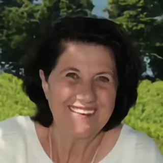 Gerlinde Maier, lächelnd, im weißen Oberteil vor grünen Bäumen