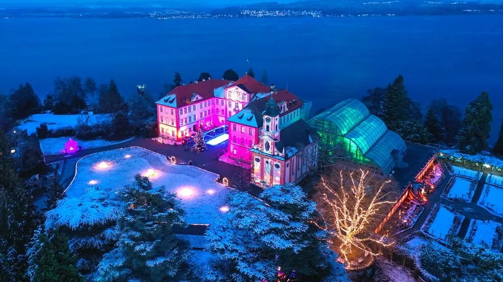 Luftaufnahme der winterlichen Insel Mainau mit bunt beleuchtetem Schloss beim Christmas Garden
