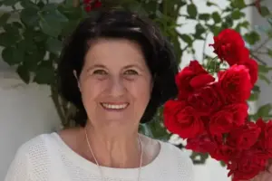 Gerlinde Maier lächelt vor einem Strauch mit roten Rosen
