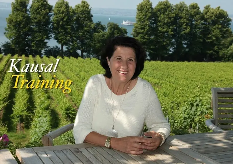 Gerlinde Maier sitzt lächelnd an einem Holztisch vor Weinbergen, dahinter der Bodensee