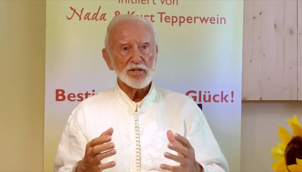 Kurt Tepperwein in weißem Gewand gestikuliert vor einem Banner mit der Aufschrift „Nada & Kurt Tepperwein“