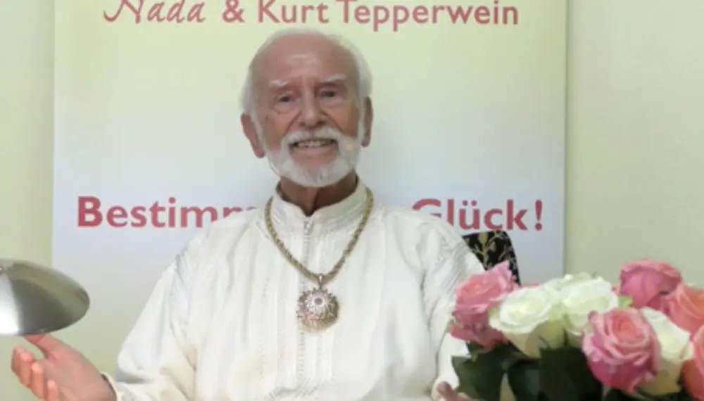 Kurt Tepperwein in weißem Gewand vor einem Banner, rechts ein Rosenstrauß
