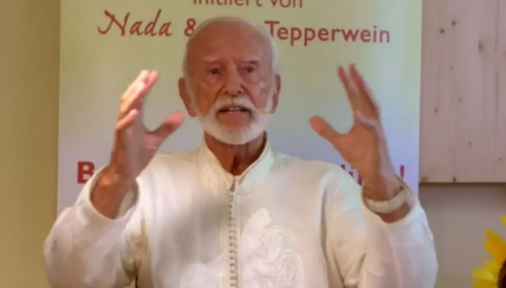 Kurt Tepperwein in weißem Gewand gestikuliert mit erhobenen Händen vor einem Banner