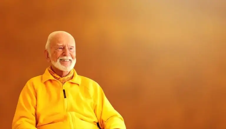 Kurt Tepperwein in gelber Jacke lächelt vor warmem orangefarbenem Hintergrund