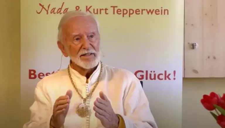 Kurt Tepperwein in weißem Gewand spricht vor einem Banner mit der Aufschrift „Nada & Kurt Tepperwein“
