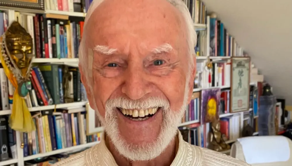 Kurt Tepperwein lacht herzlich vor einem Bücherregal