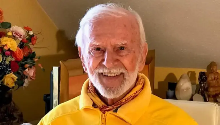 Kurt Tepperwein in gelber Jacke lacht in die Kamera, links ein bunter Blumenstrauß
