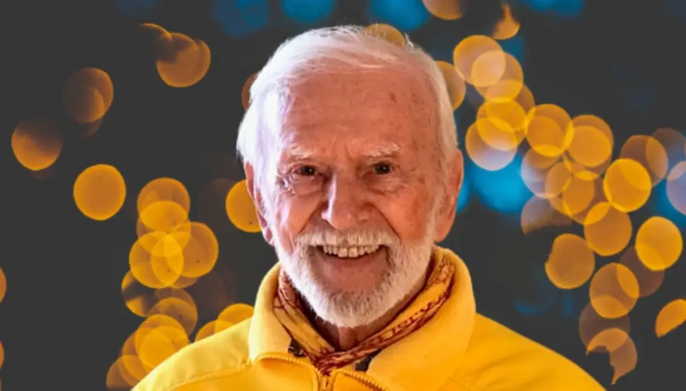 Kurt Tepperwein lacht vor dunklem Hintergrund mit goldenen Lichtpunkten