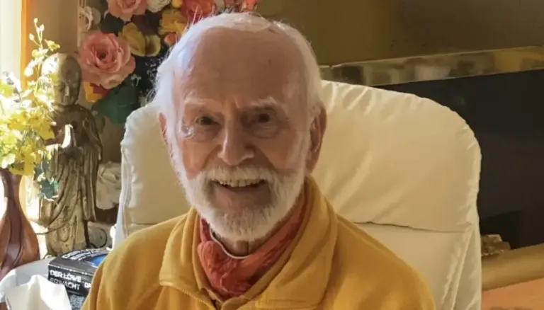 Kurt Tepperwein mit rotem Halstuch lacht in einem hellen Sessel, links Blumen