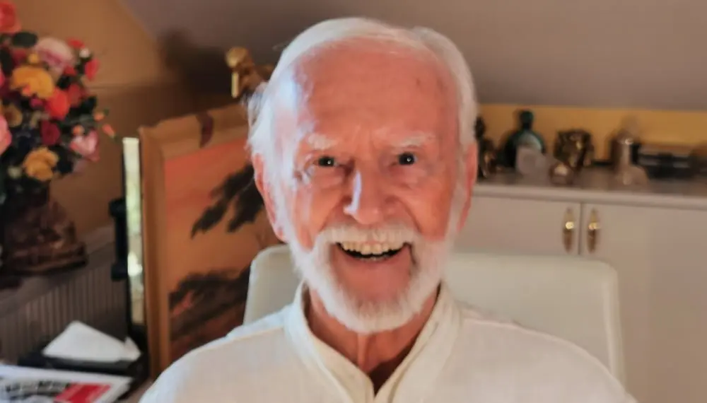 Kurt Tepperwein lacht in die Kamera, im Hintergrund ein Blumenstrauß