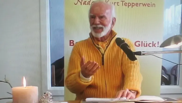 Kurt Tepperwein in gelbem Pullover spricht am Mikrofon, vorne eine brennende Kerze