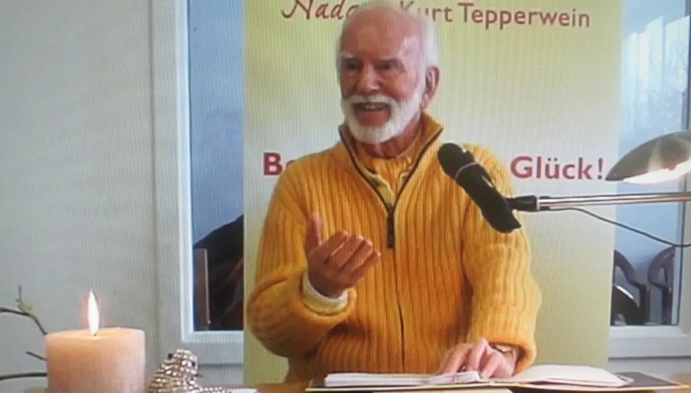 Kurt Tepperwein in gelbem Pullover spricht am Mikrofon, vorne eine brennende Kerze