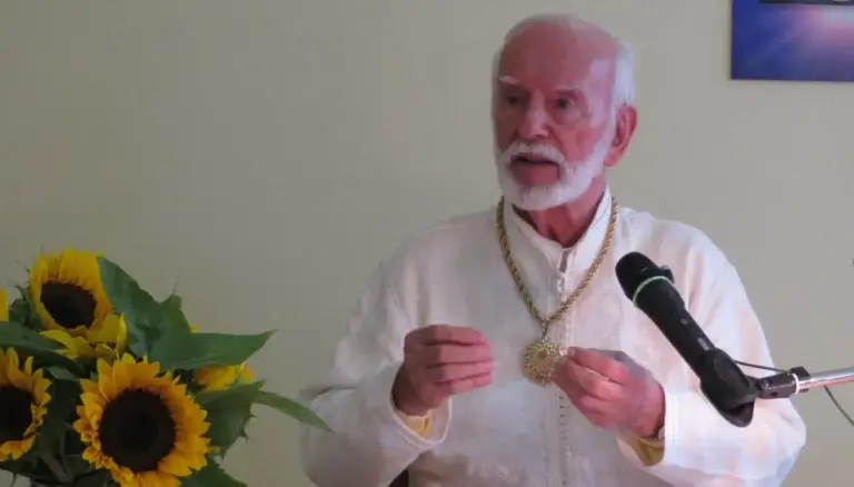 Kurt Tepperwein in weißem Gewand spricht am Mikrofon, vorne Sonnenblumen