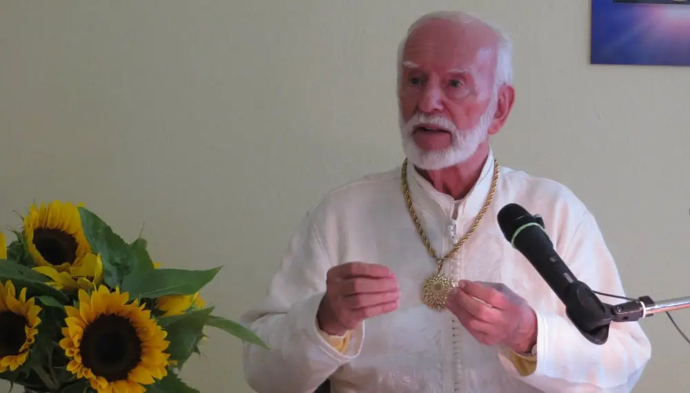 Kurt Tepperwein in weißem Gewand spricht am Mikrofon, vorne Sonnenblumen