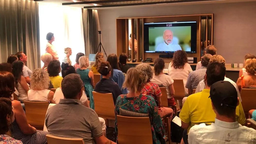 Voll besetzter Seminarraum, Kurt Tepperwein ist per Zoom auf einem großen Bildschirm zugeschaltet